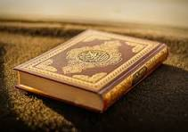 An open mushaf on a wooden rehal with morning light across the page